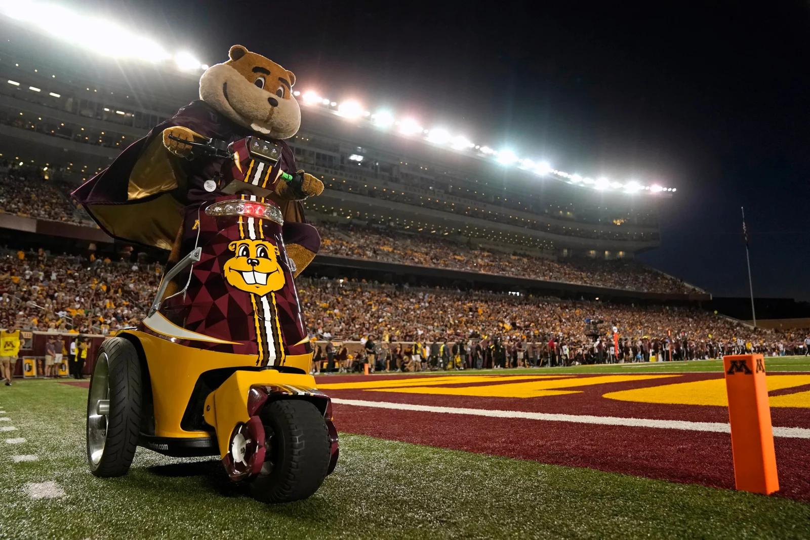 a mascot gopher rides a motor bike during a football game